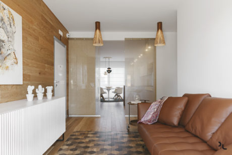 Modern, open-plan living space with sleek wooden accents, pendant lighting, and a leather sofa.