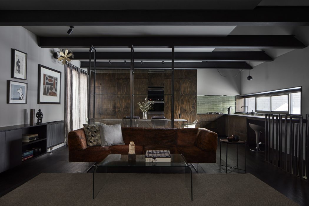 Modern industrial-style living room with dark wood panels, exposed beams, and glass coffee table.