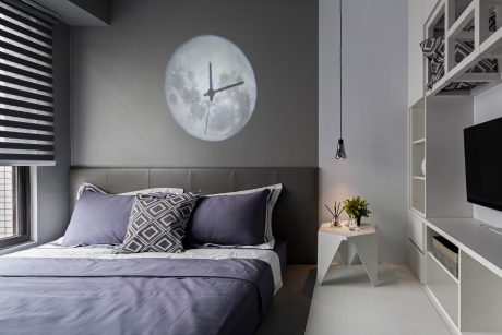 Modern bedroom with large moon-shaped clock, grey walls, and minimalist furnishings.