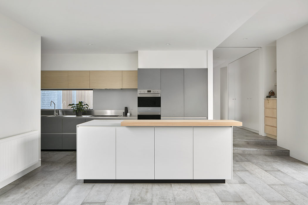 Minimalist kitchen design with sleek gray and light wood cabinetry, center island, and tile flooring.