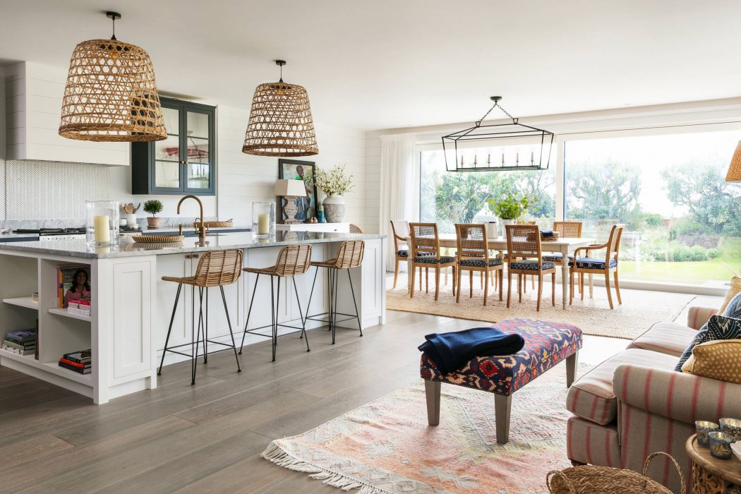 Spacious open-concept kitchen with large windows, woven pendant lamps, and a rustic wood dining table.