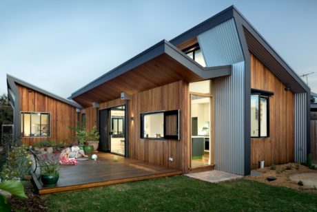 Modern single-story house with sloping roof, wooden siding, and large glass windows.