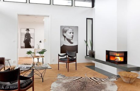 A modern living room with large windows, artwork, and a fireplace set against a clean, white backdrop.