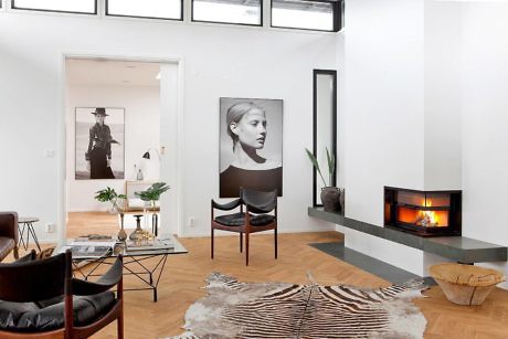 A modern living room with large windows, artwork, and a fireplace set against a clean, white backdrop.