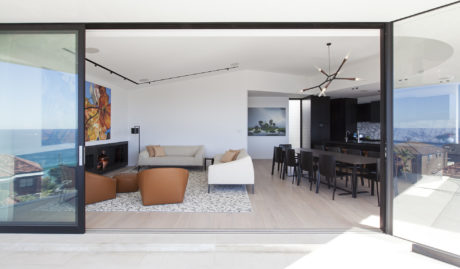 A modern, open-concept living area with floor-to-ceiling windows, sleek furnishings, and a striking chandelier.