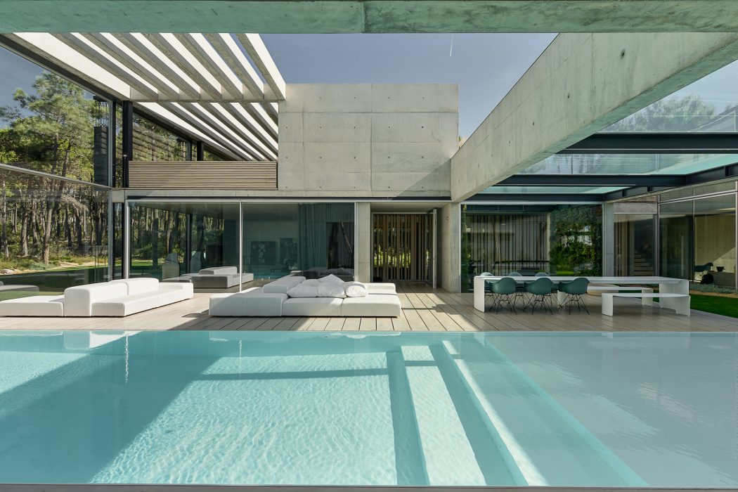 A modern, open-plan house with a sleek concrete exterior, large windows, and a serene swimming pool.