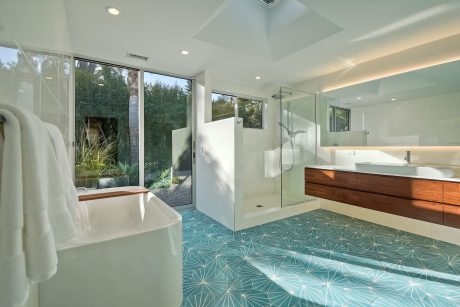 Striking modern bathroom with a glass-enclosed shower, wooden vanity, and patterned tile floor.