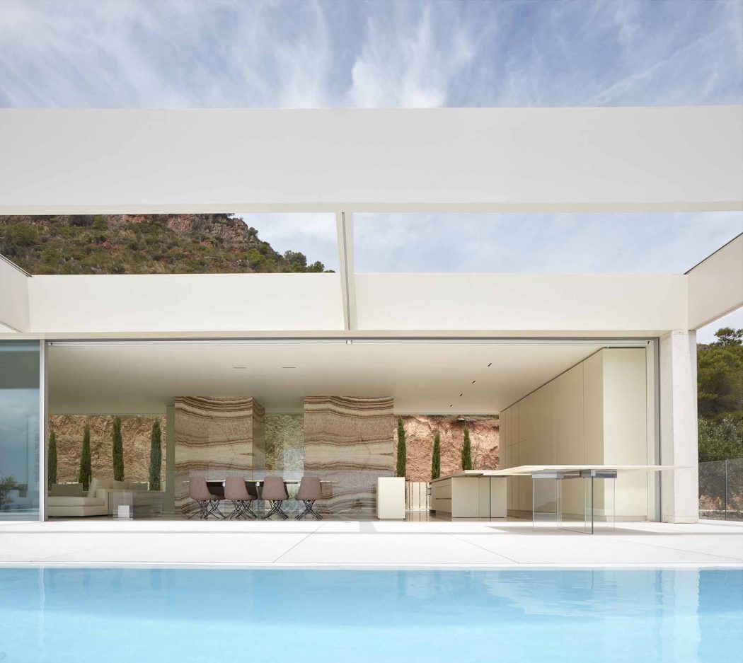A modern, minimalist outdoor living space with a pool, benches, and rock formations.