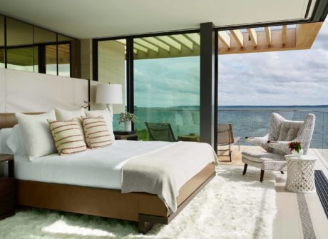 Spacious bedroom with floor-to-ceiling windows overlooking the ocean, modern furnishings.