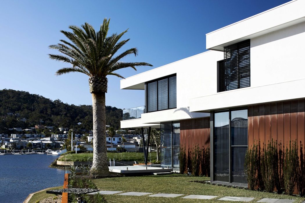 Modern, waterfront house with sleek, white exterior, large windows, and a palm tree.