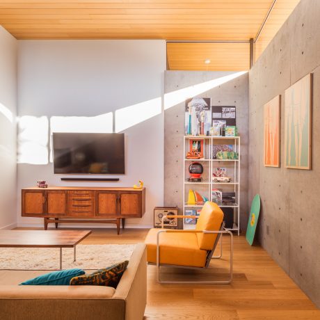 Warm, modern living room with concrete walls, wooden ceiling, and mid-century furnishings.