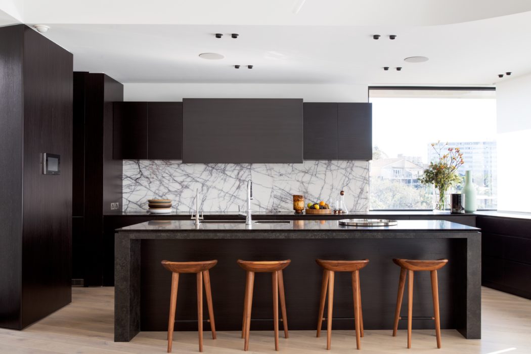 Sleek, modern kitchen with dark cabinets, marble backsplash, and wood bar stools.
