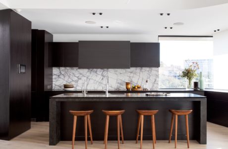 Sleek, modern kitchen with dark cabinets, marble backsplash, and wood bar stools.