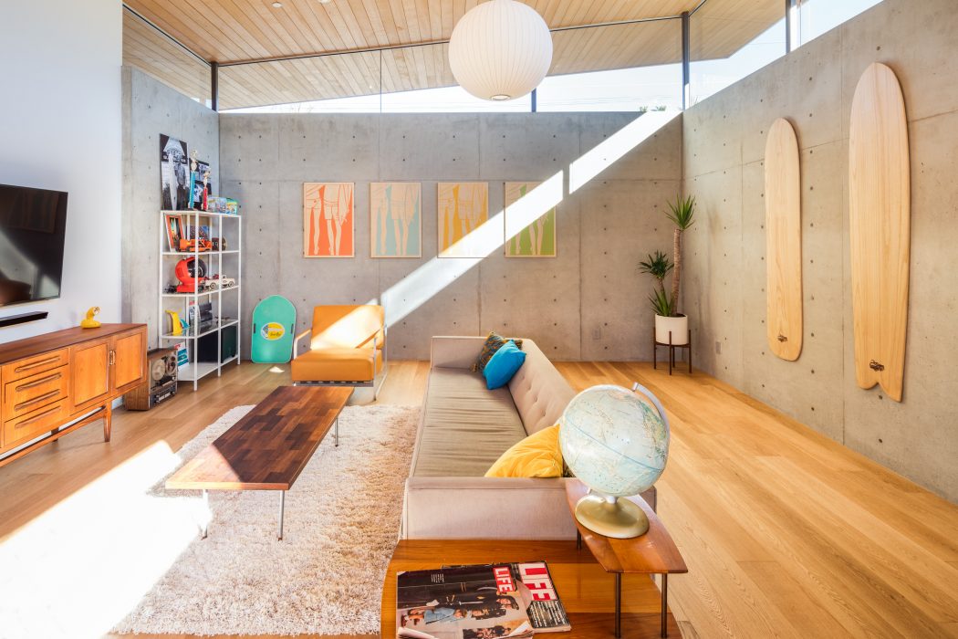 A modern living room with wooden ceiling, concrete walls, and vibrant artwork.