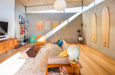 A modern living room with wooden ceiling, concrete walls, and vibrant artwork.