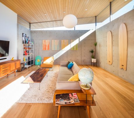 A modern living room with wooden ceiling, concrete walls, and vibrant artwork.