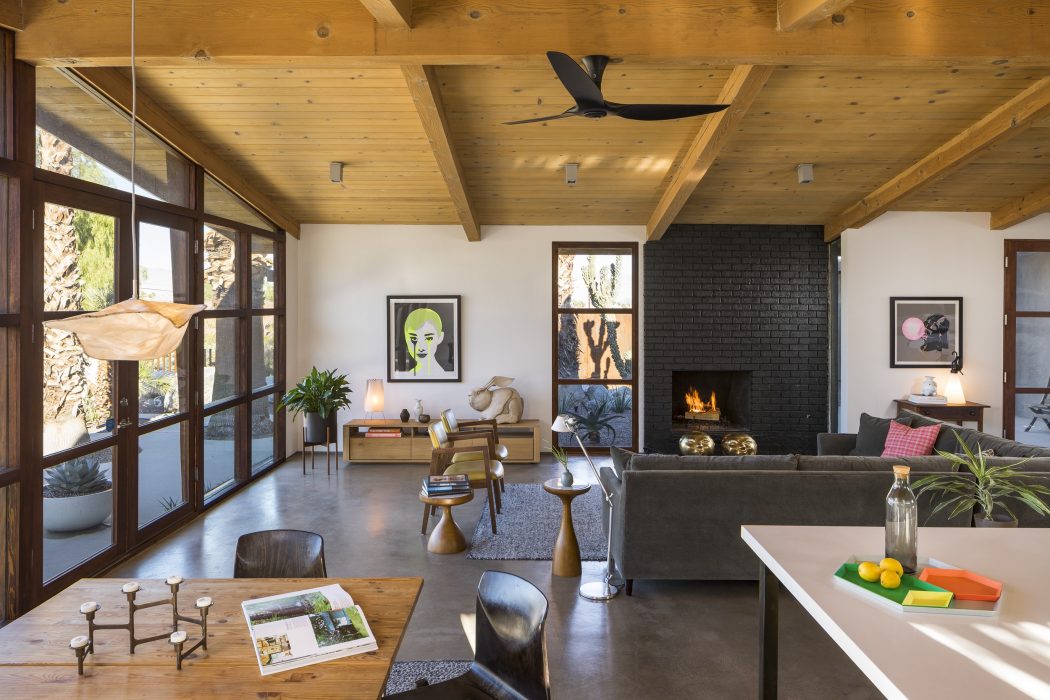 Rustic wooden beams, sleek concrete floors, and a striking black brick fireplace create a cozy, modern atmosphere.