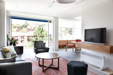 Bright, minimalist living space with large window, patterned rug, and modern wood furniture.