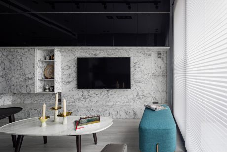 Sleek, modern living space with marble TV wall, round coffee table, and turquoise armchair.