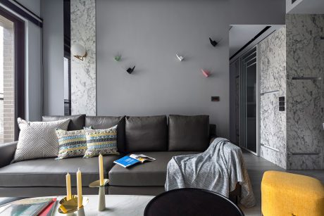 Modern minimalist living room with sleek gray sofa, patterned pillows, and abstract wall decor.