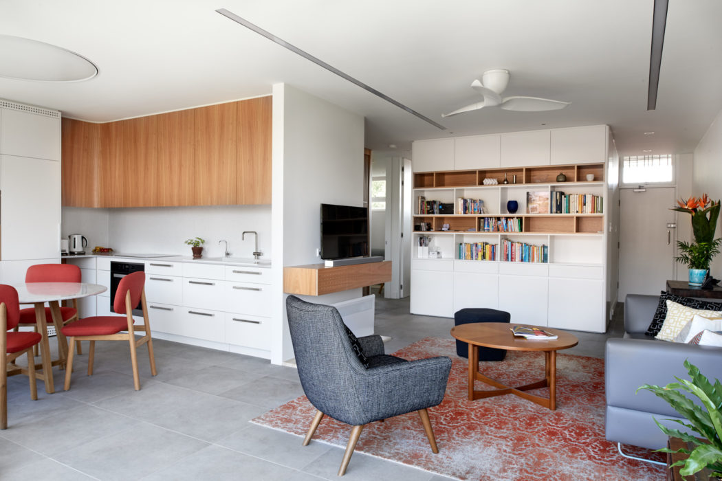 Bright, modern open-plan room with wood and white furniture, bookshelf, and plush rug.