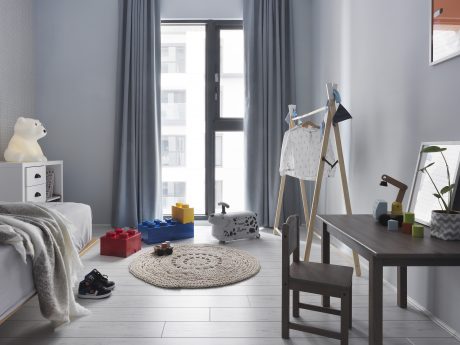 A cozy children's bedroom with minimalist furniture, large windows, and a plush rug.