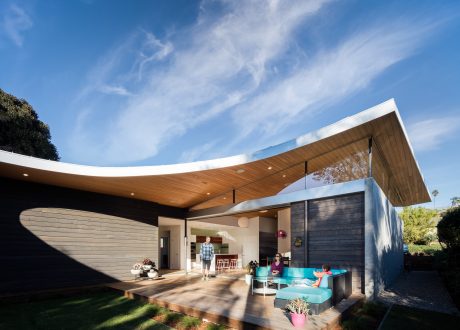 Modern curved roofline with timber cladding, open living space, and patio furniture.
