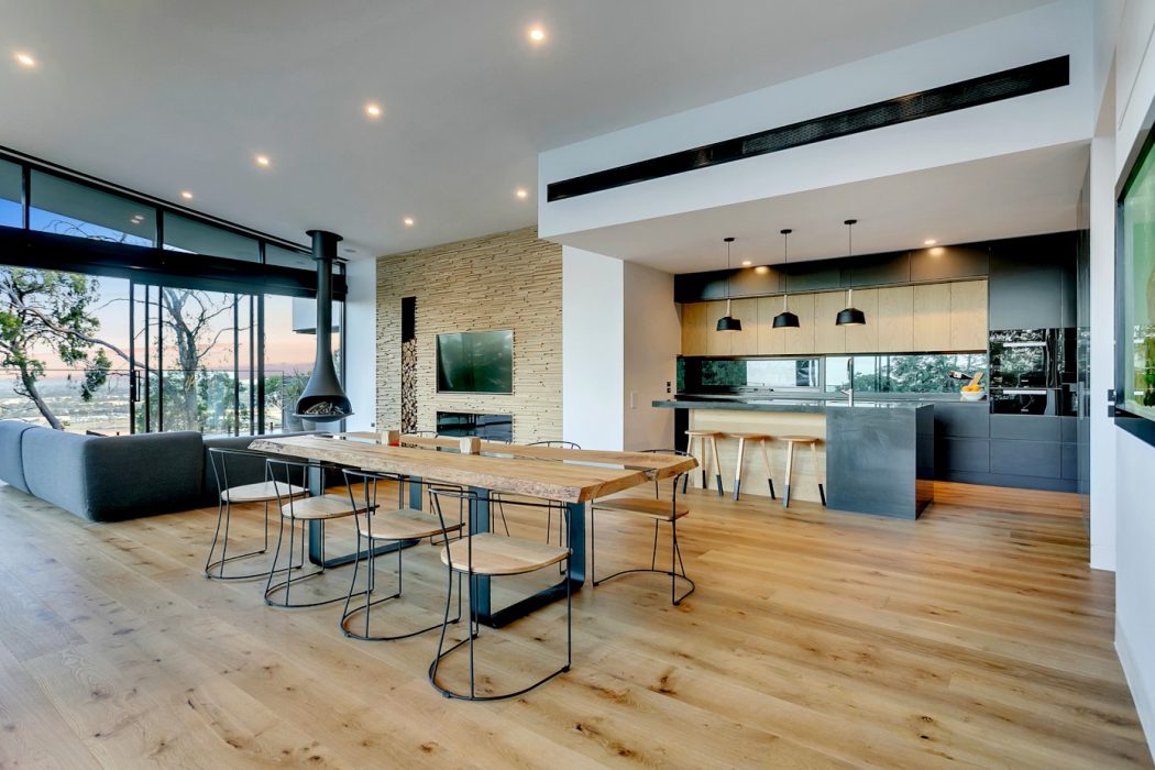 Expansive modern interior with wooden floors, stone wall, and sleek kitchen design.