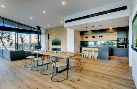 Expansive modern interior with wooden floors, stone wall, and sleek kitchen design.