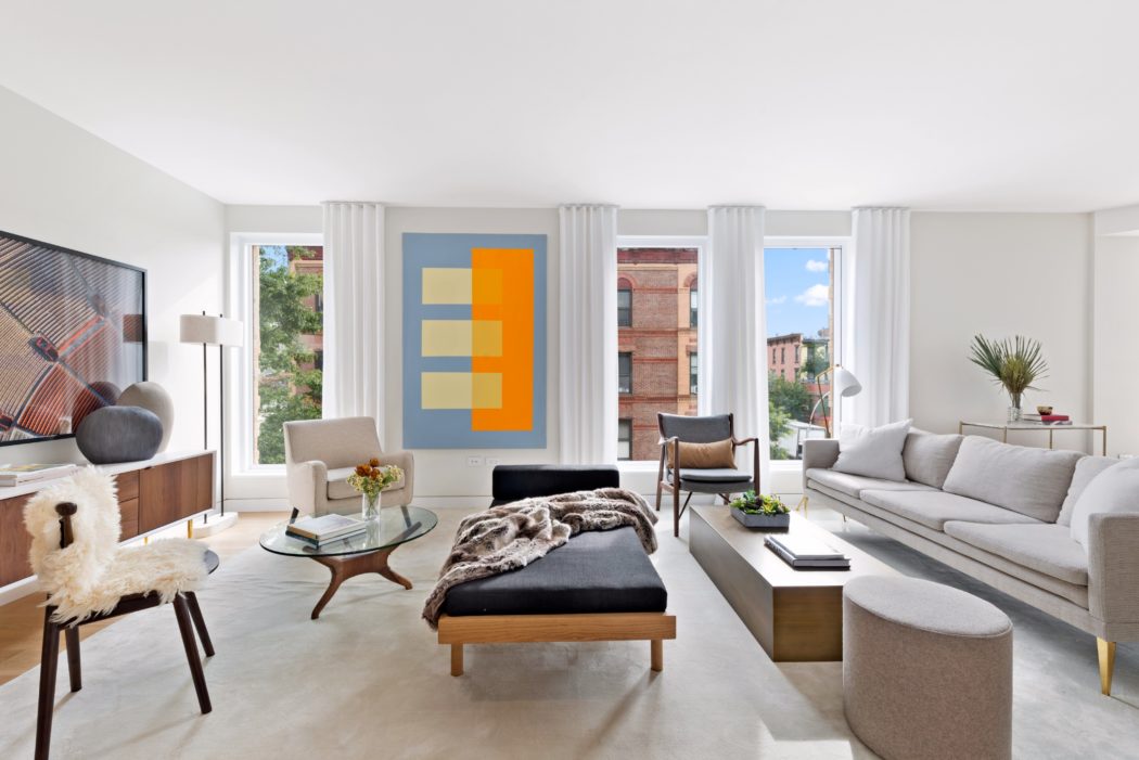 Contemporary living space with minimalist furnishings, statement artwork, and large windows offering city views.