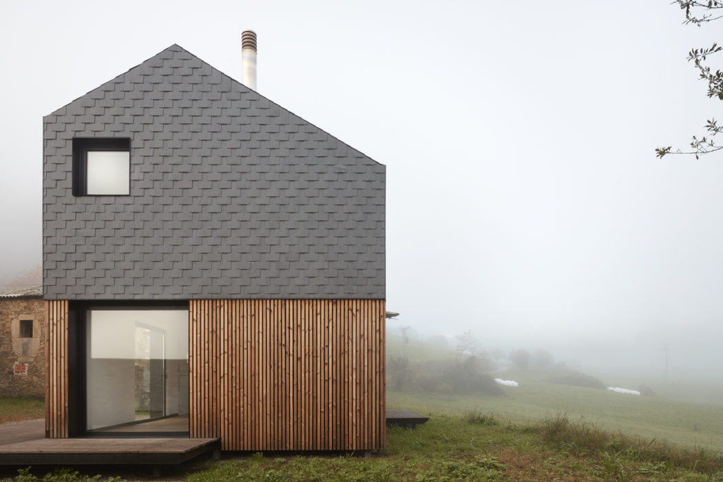A modern, wood-clad house with a gray shingled roofline stands in a foggy, grassy field.