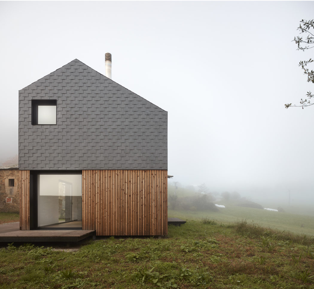 A modern, wood-clad house with a gray shingled roofline stands in a foggy, grassy field.