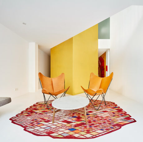 A modern, minimalist interior with vibrant yellow and green walls, leather butterfly chairs, and a colorful patterned rug.