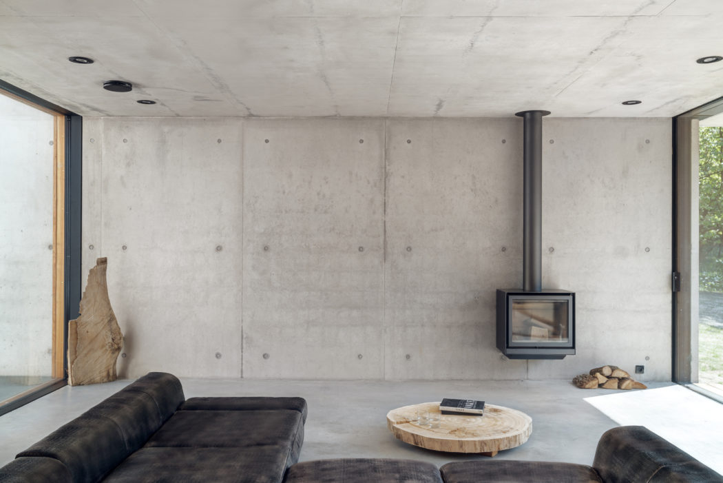 Minimalist living room with exposed concrete walls, wood-burning stove, and stone coffee table.