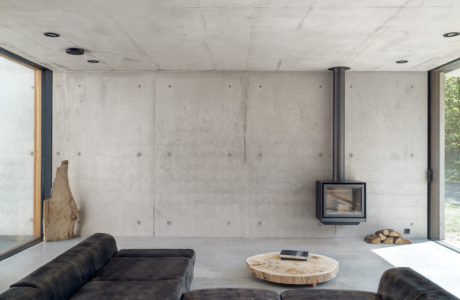 Minimalist living room with exposed concrete walls, wood-burning stove, and stone coffee table.