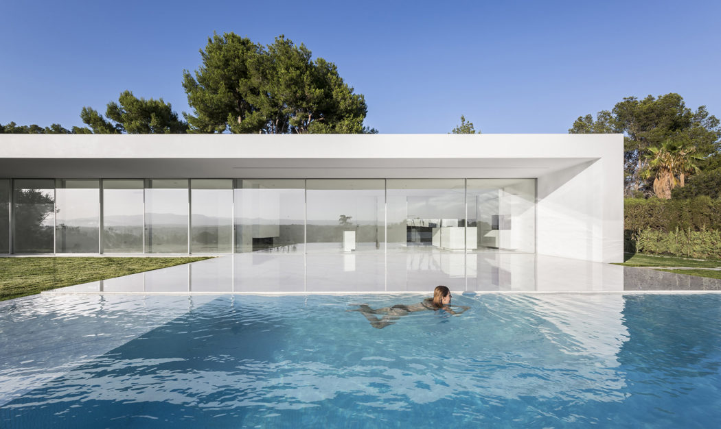 An expansive glass-walled home with a serene infinity pool and lush natural surroundings.