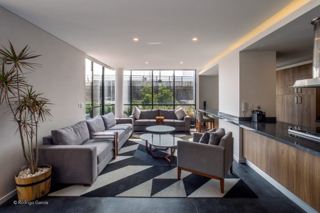 A modern, open-concept living room with large windows, plush gray sofas, and a patterned rug.