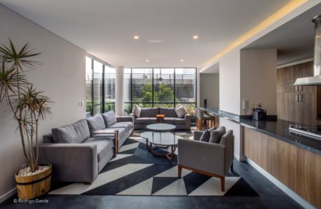 A modern, open-concept living room with large windows, plush gray sofas, and a patterned rug.