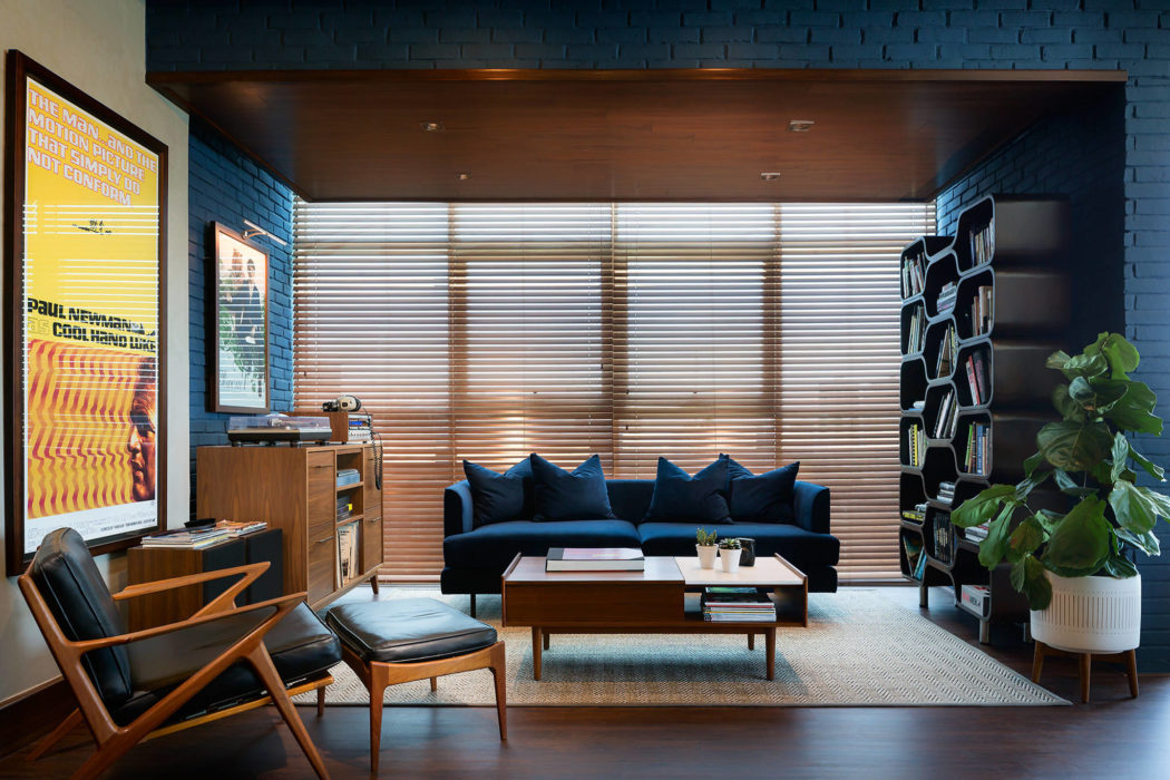 Stylish mid-century modern living room with blue sofa, wooden furnishings, and brick walls.