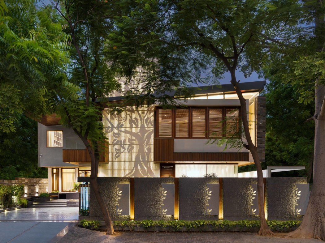 Modern, nature-inspired architecture with intricate wooden screens, lighting features, and lush greenery surrounding the residential structure.