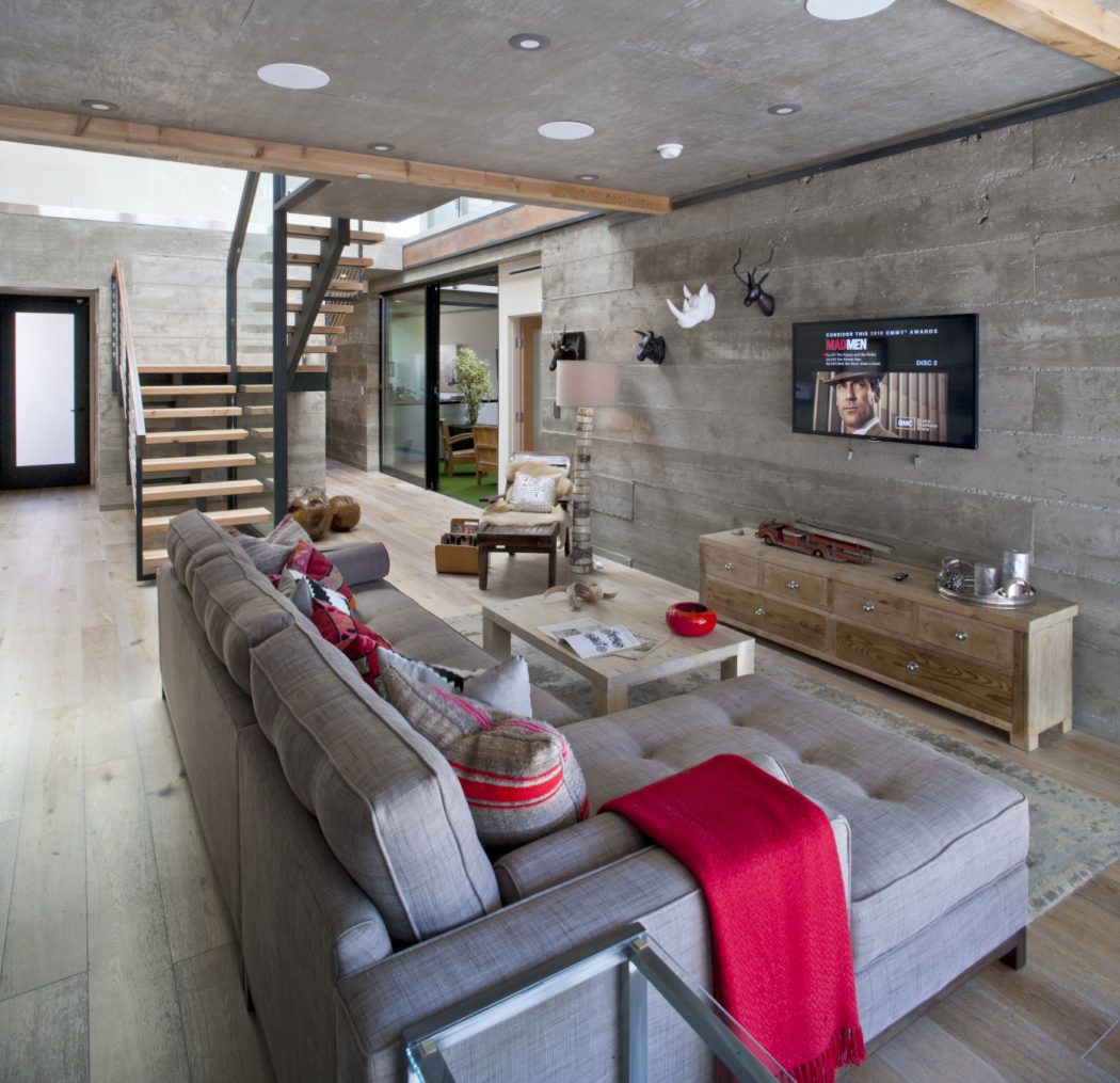 A modern, industrial-style living room with concrete walls, wooden accents, and a cozy seating area.