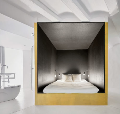 Minimalist bedroom with concrete alcove and yellow accent, modern bathroom visible.