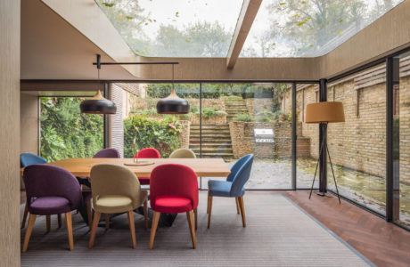 Modern open-plan dining space with colorful chairs, pendant lights, and garden view.