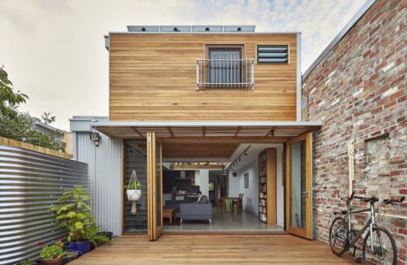 A modern two-story house with a wooden exterior, balcony, and large sliding glass doors opening to a deck.