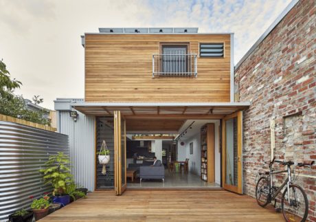 A modern two-story house with a wooden exterior, balcony, and large sliding glass doors opening to a deck.