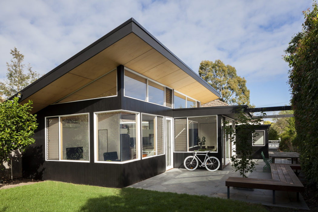A modern, minimalist home with a slanted roof, large windows, and a bicycle on the patio.
