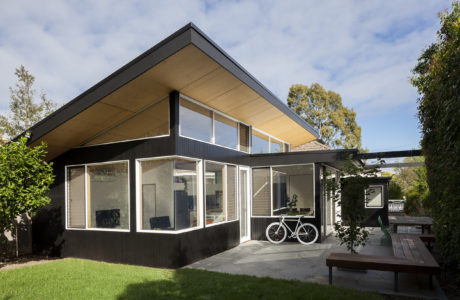 A modern, minimalist home with a slanted roof, large windows, and a bicycle on the patio.