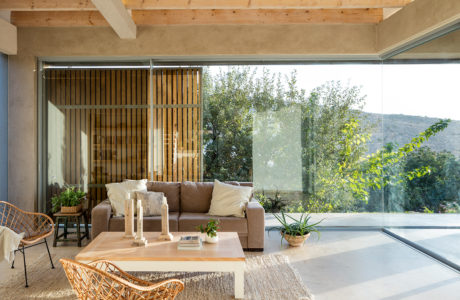 Warm, rustic living room with wood-beamed ceiling, glass walls, and modern furnishings.