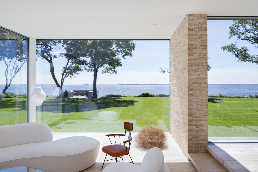 Expansive waterfront view through floor-to-ceiling glass, framed by brick accent wall.