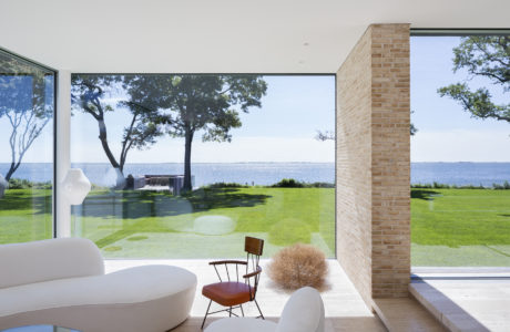 Expansive waterfront view through floor-to-ceiling glass, framed by brick accent wall.